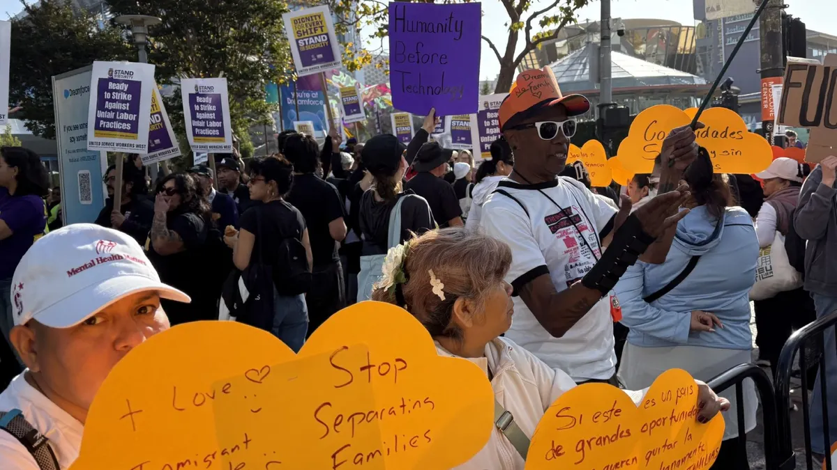 A diverse group of people hold signs in various colors and written in both English and Spanish outside of the 2026 Dreamforce conference.