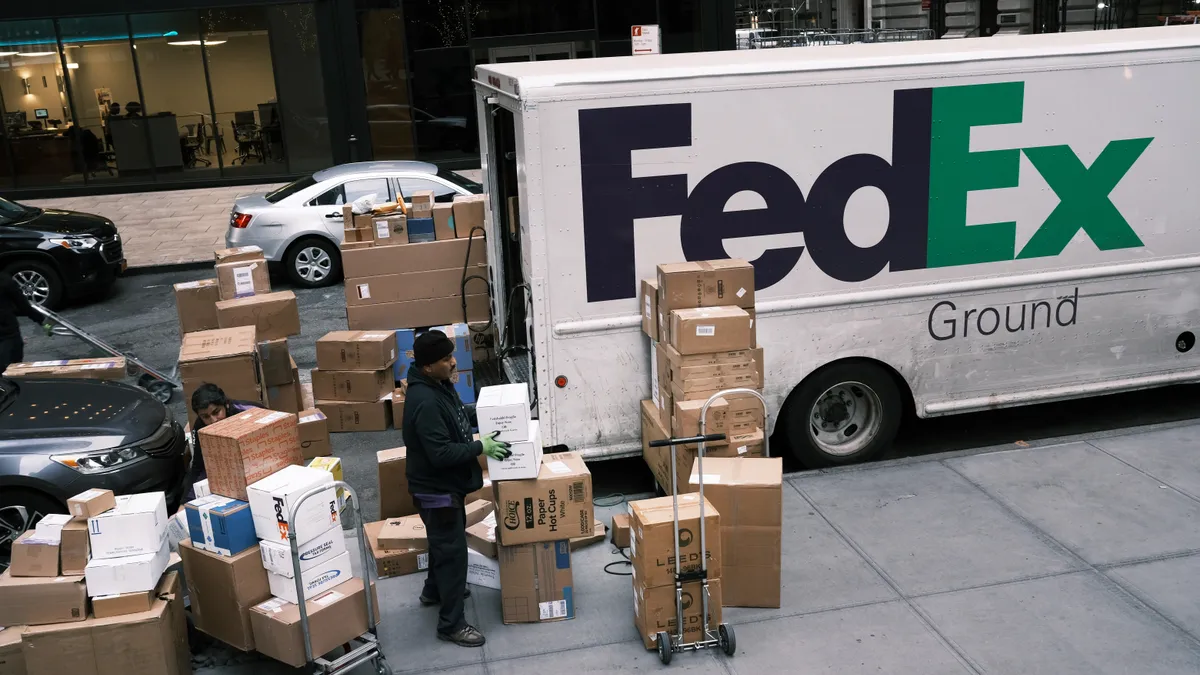 A person handles a pile of boxes on the sidewalk next to a truck emblazoned with "FedEx Ground."