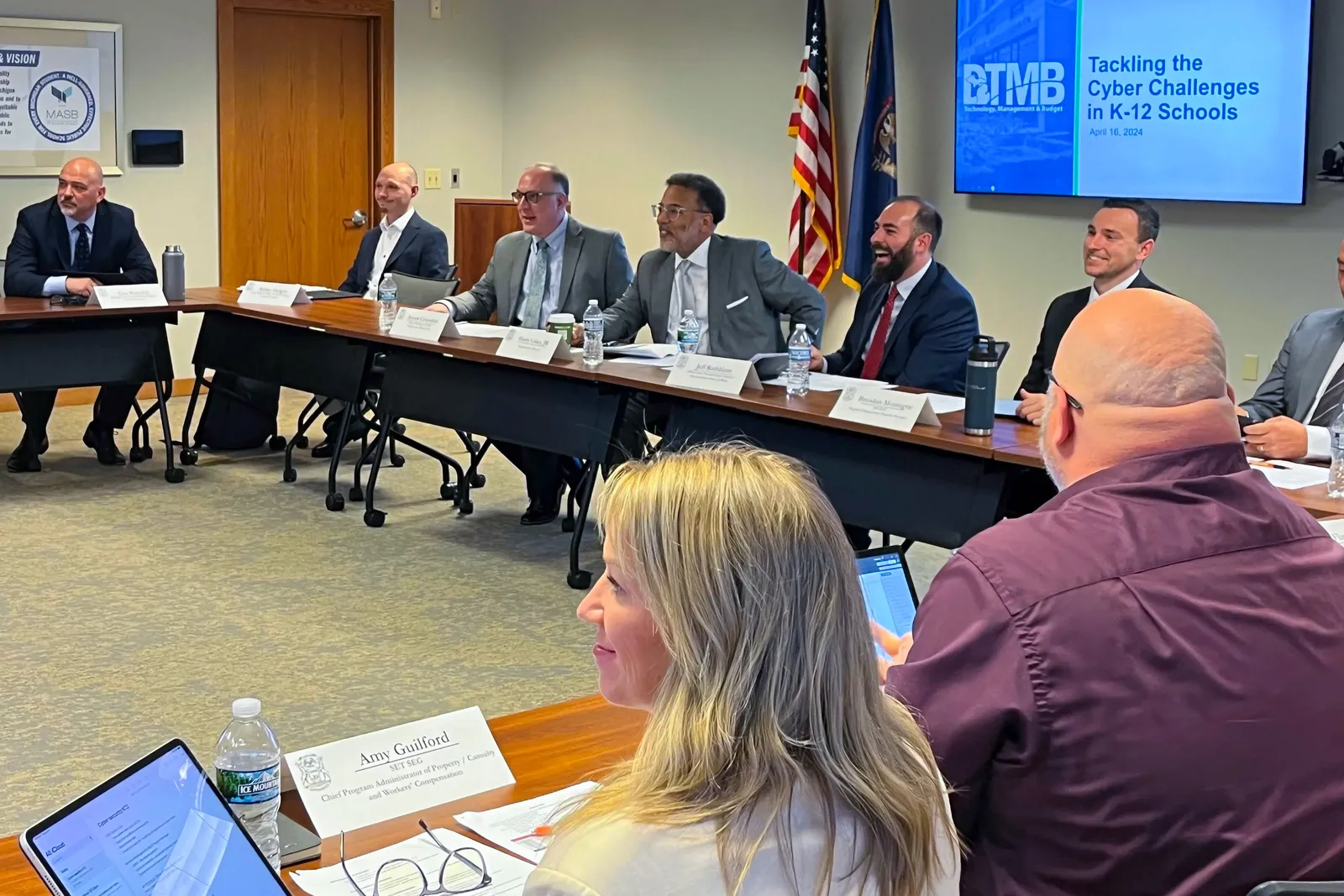 State and national cybersecurity professionals sit in on a roundtable discussion as a screen in the background reads: “Tackling the cyber challenges in K-12 Schools.”