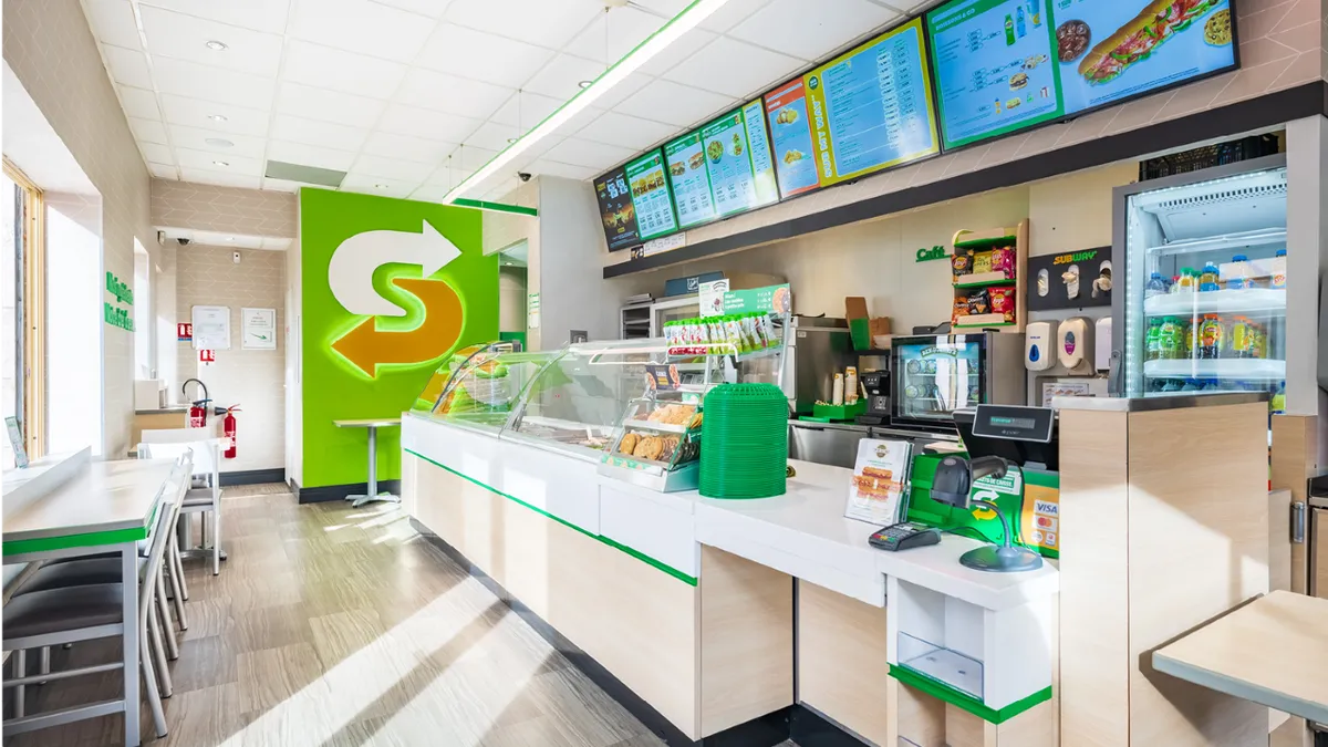 A Subway restaurant interior with white and green countertops and digital menu boards.