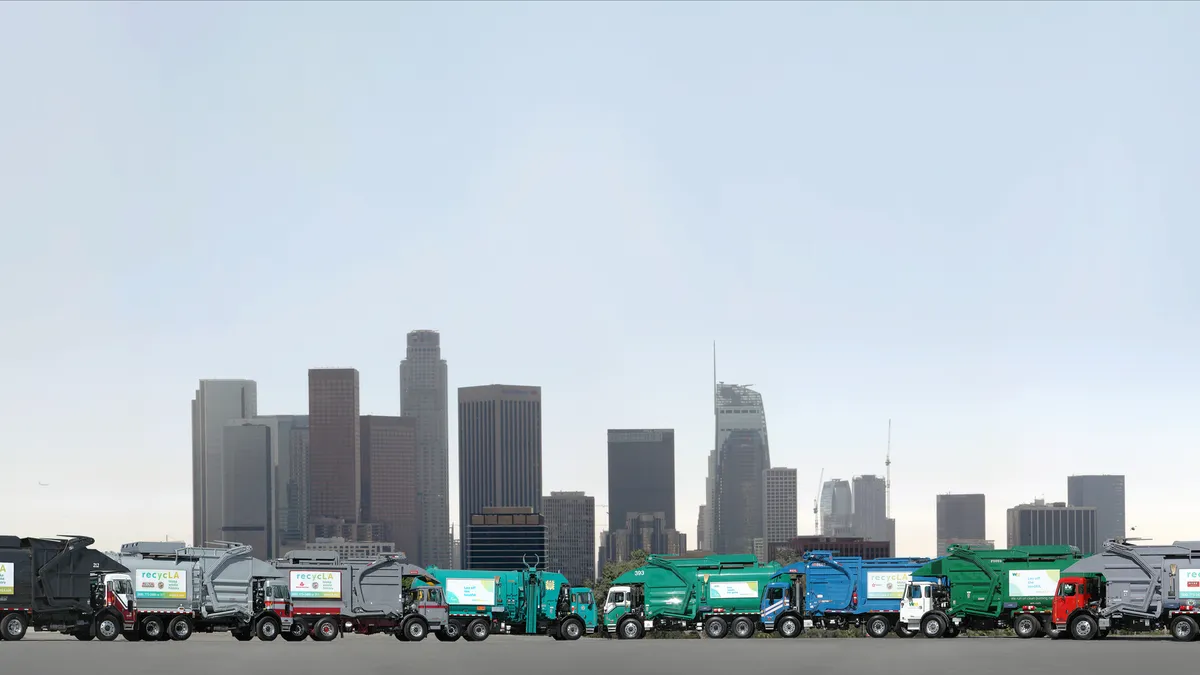 A row of garbage trucks parked in front of the Los Angeles skyline