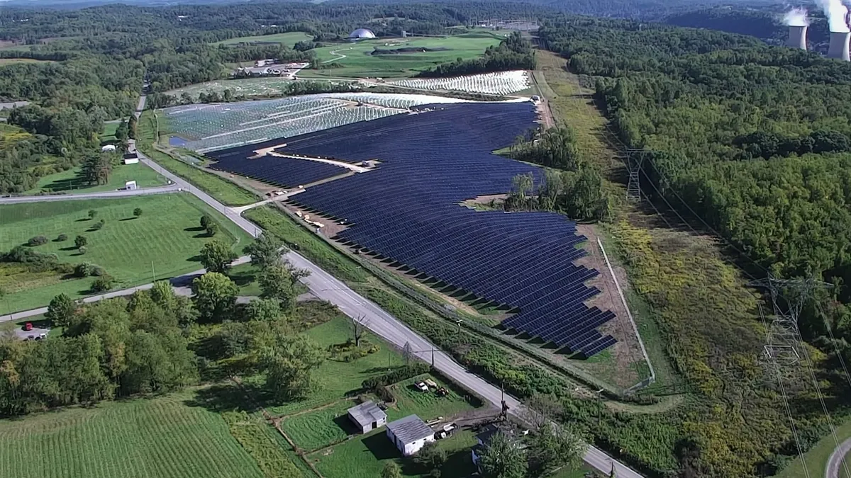 An aerial view of a solar farm next to power lines and trees.