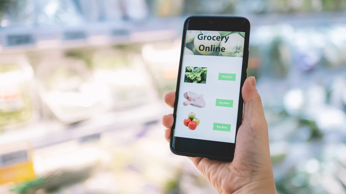 Close-up of a hand holding a phone with a grocery app open while inside a supermarket.