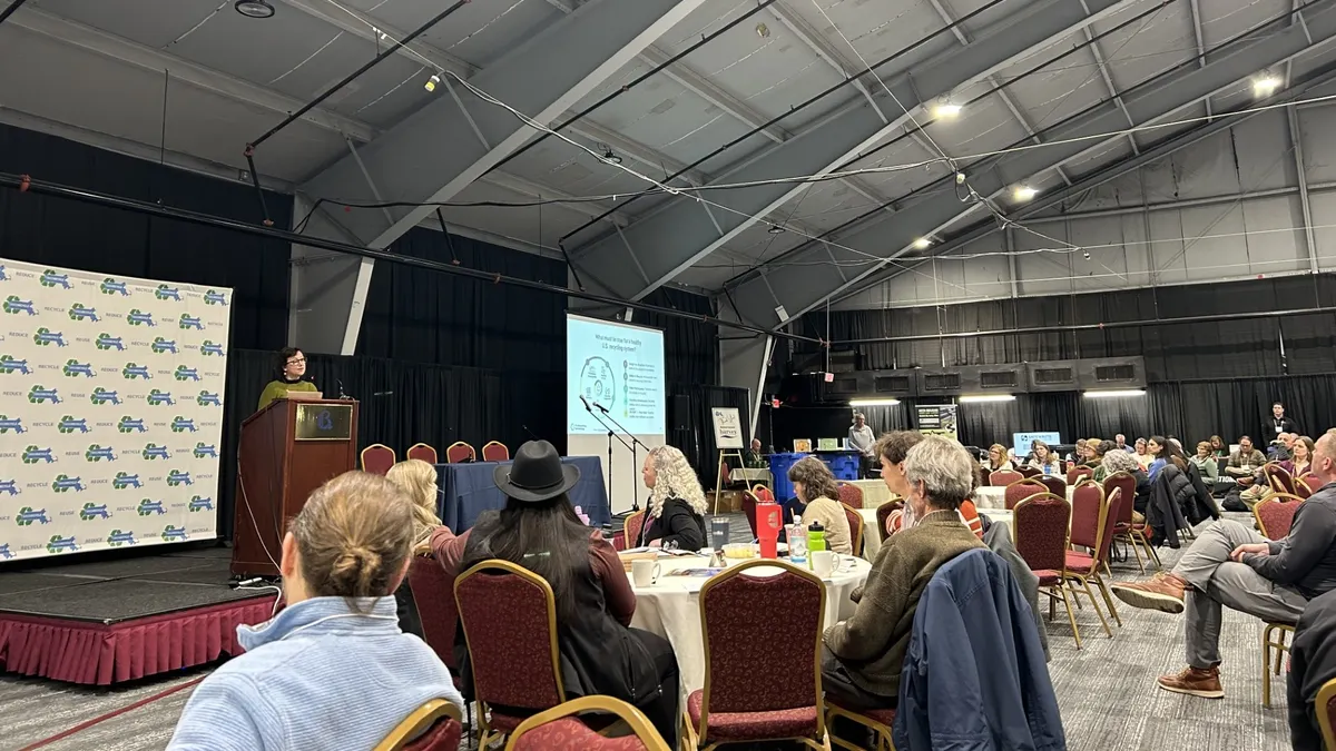 Recycling Partnership CEO Keefe Harrison stands behind a podium on a small stage in front of a crowd of seated people