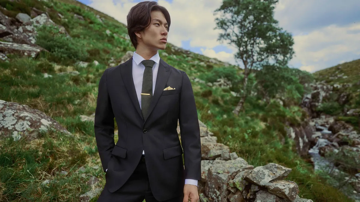 A person wearing a suit in a green landscape.