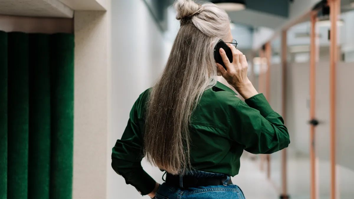 An older woman speaks on the phone in a darkened hallway