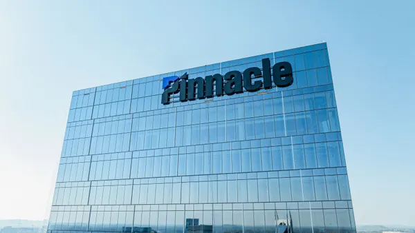 A glass office building with the word "Pinnacle" and its logo on the exterior is seen from high above Nashville's downtown.