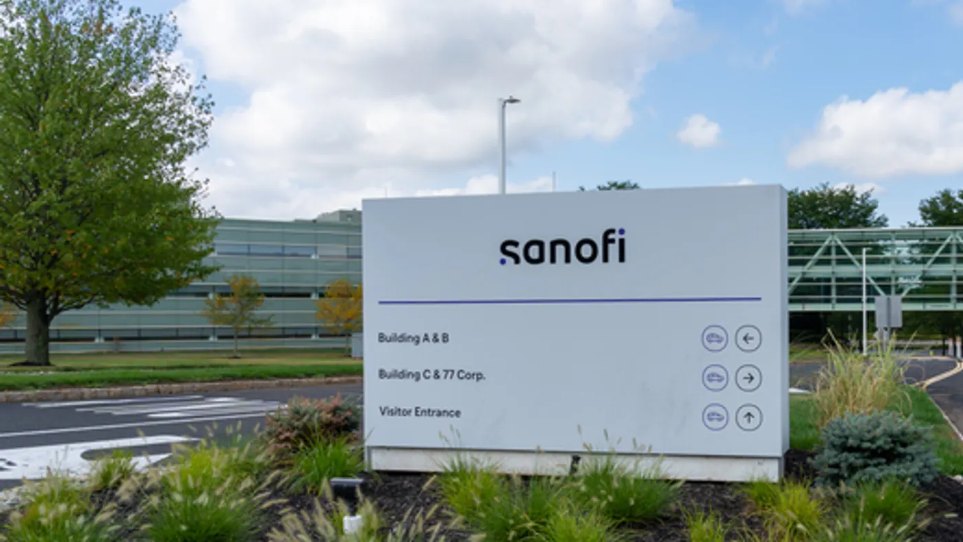 A white sign bears the word Sanofi at a road entrance to an office building.