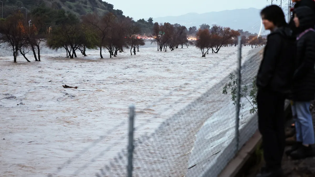 A group of people stand behind a gate as a river rushes in front of them