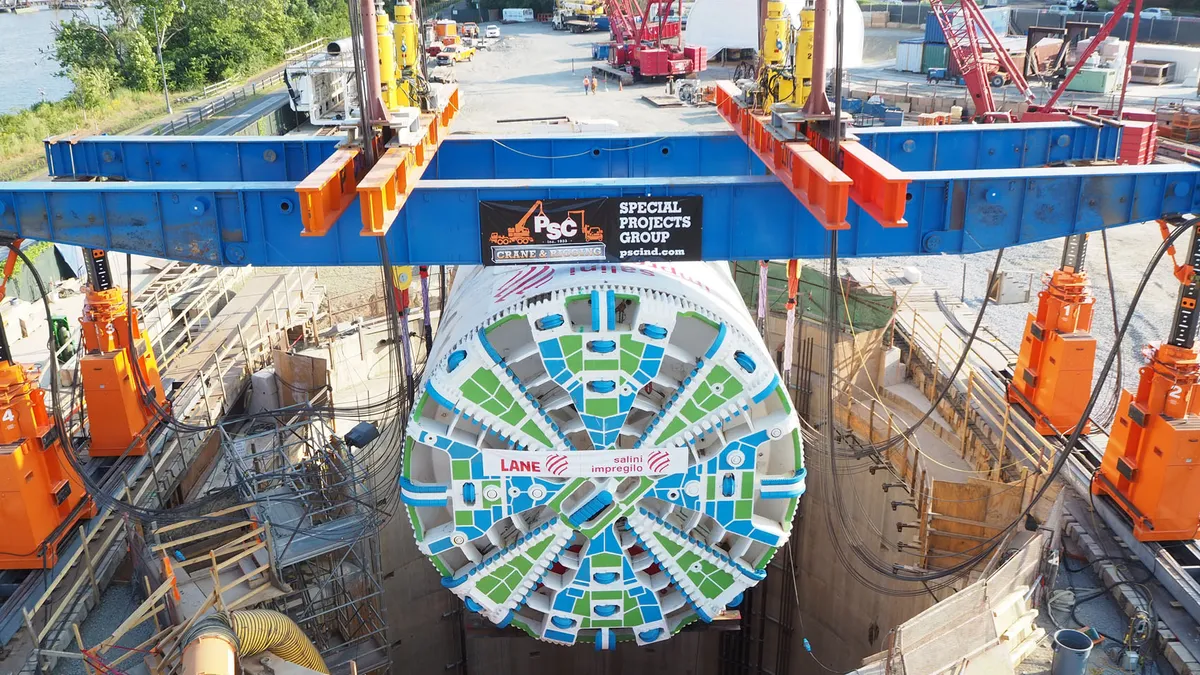 A massive round white boring machine is lowered into a concrete-lined hole.