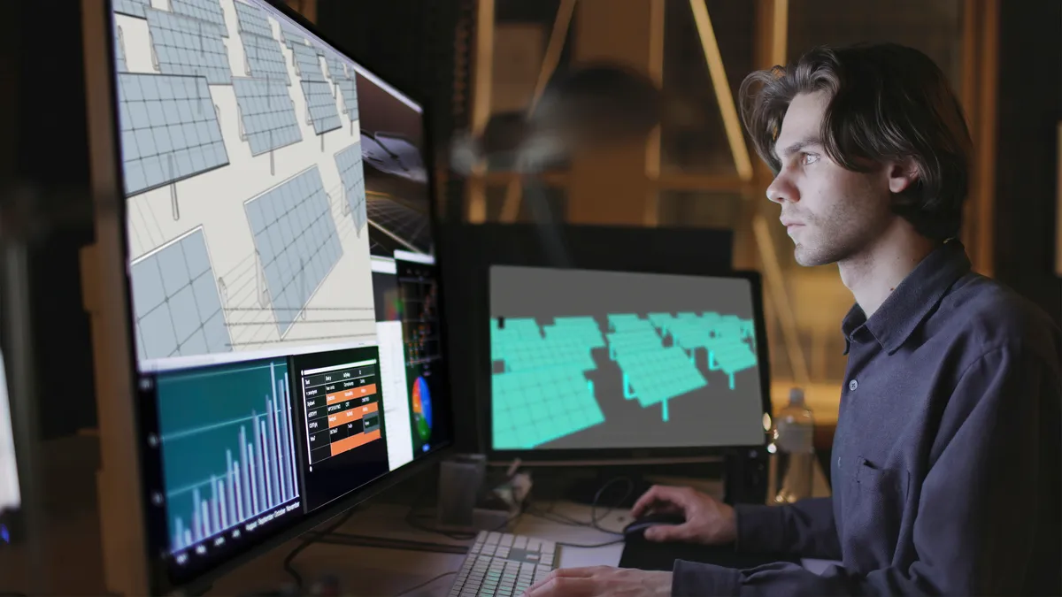 A closeup shot of a young man works at a computer screen on a software looking at the design of a solar panel array in CAD with data.