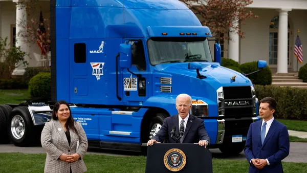 Former President Biden giving a speech on the White House South Lawn with a semi truck parked behind him.