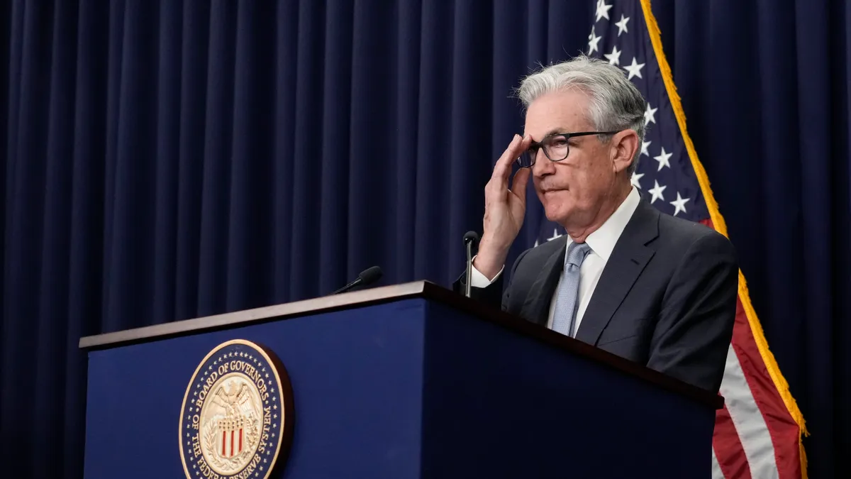 Fed Reserve Chair Jerome Powell standing at podium and adjusting his glasses with his hand.