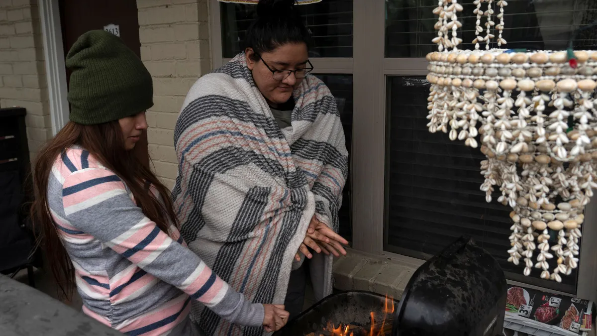 People warm up by a barbecue grill.