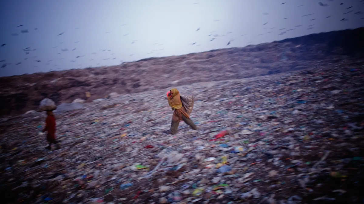 A person walks across a landfill in India with a bale of recyclables on their head.