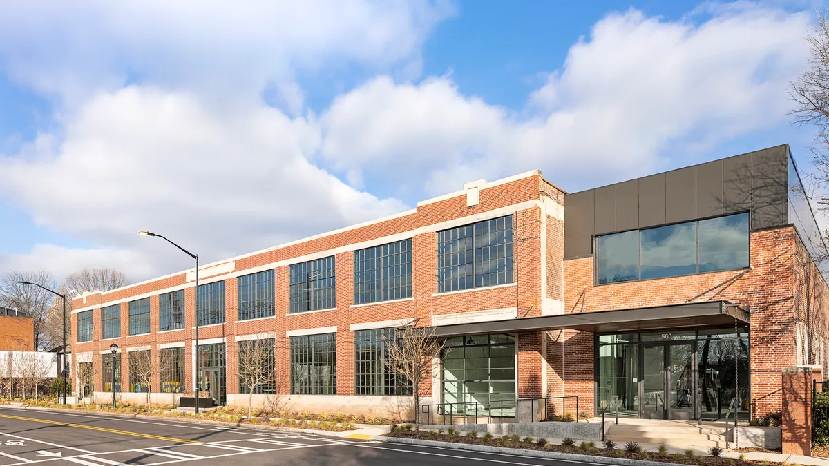 A shot of the outside of a refurbished warehouse. The light-brown-colored bricks shine next to new windows under a blue sky.