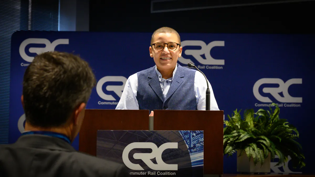 A smiling person at a podium speaking to an audience.