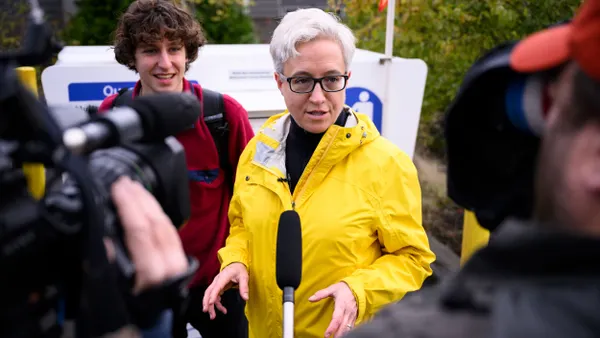 Tina Kotek, wearing a yellow rain jacket, speaks with press.