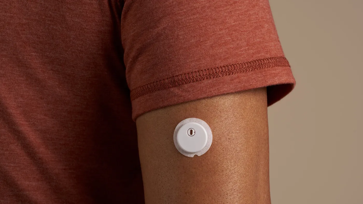 A white, round device is stuck on a person's arm below their sleeve.