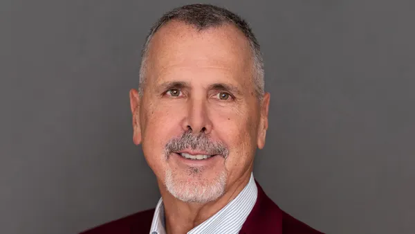 A portrait of a smiling person wearing a red blazer over a white undershirt.