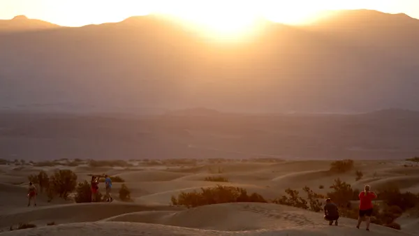People watch a hazy sun rise while standing on desert dunes.