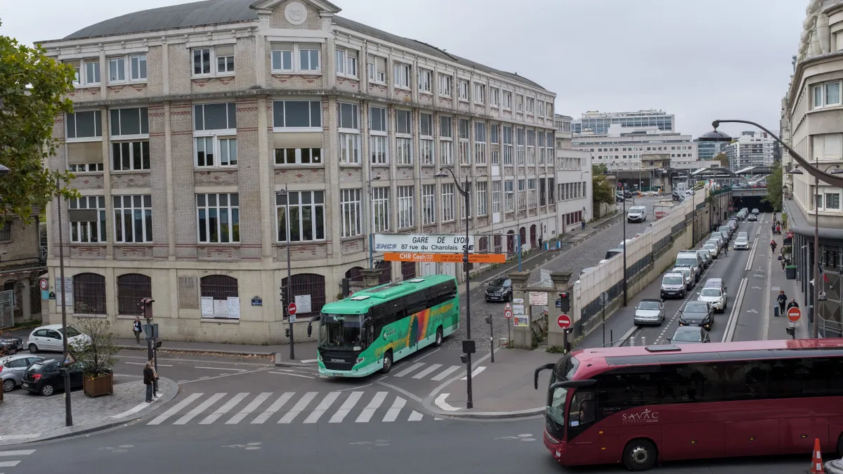 Overhead view of a street in Paris with two people waiting at a crosswalk for a bus to come through.