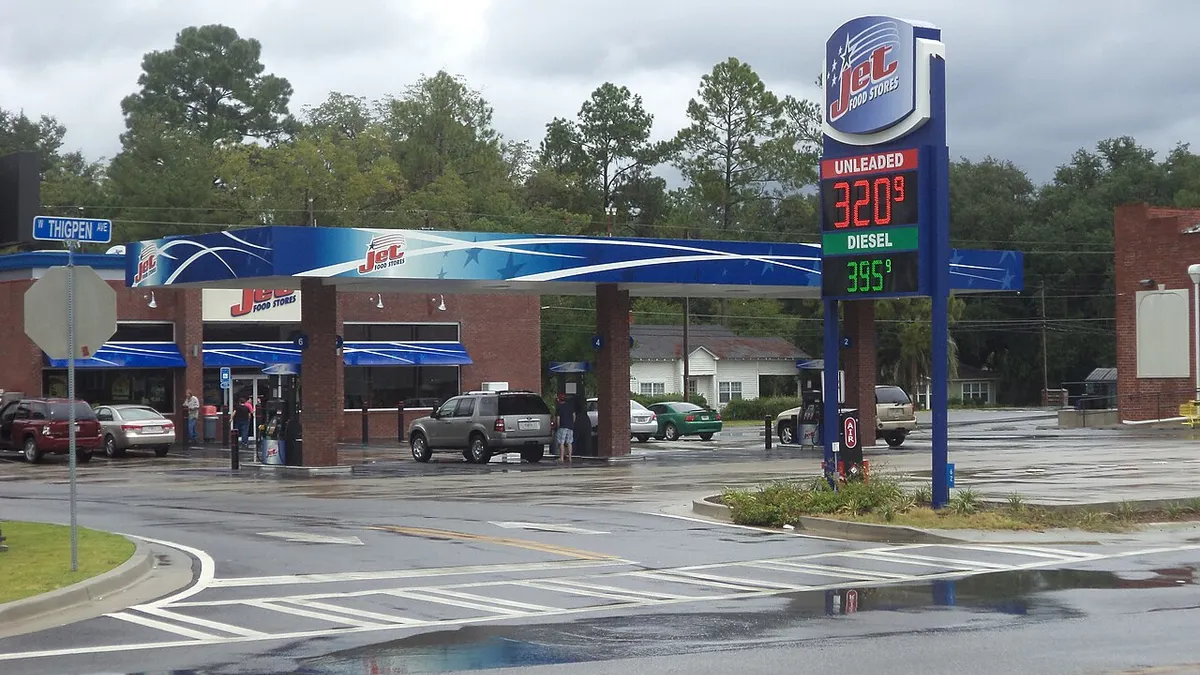 vehicles fuel up on a rainy day at a gas station and convenience store. A logo on the store, canopy and a sign out front all say "Jet Food Stores."