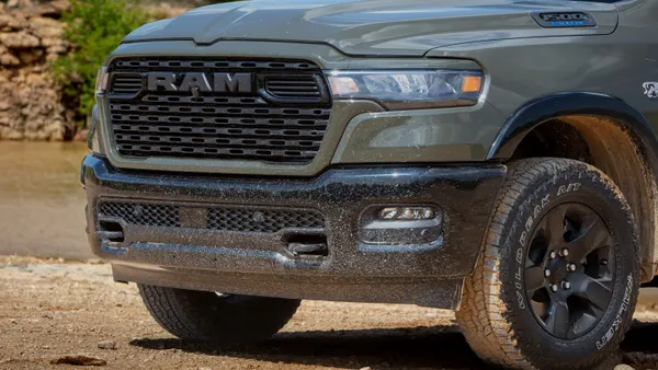 The front grill of a 2026 Ram 1500 BackCountry pickup parked outdoors on a dirt surface with mud on the tires.