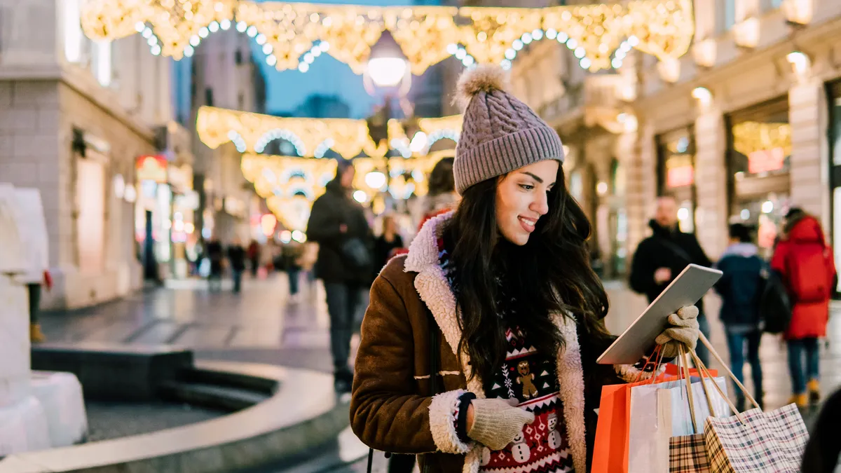 Happy young woman holding shopping bags and digital tablet