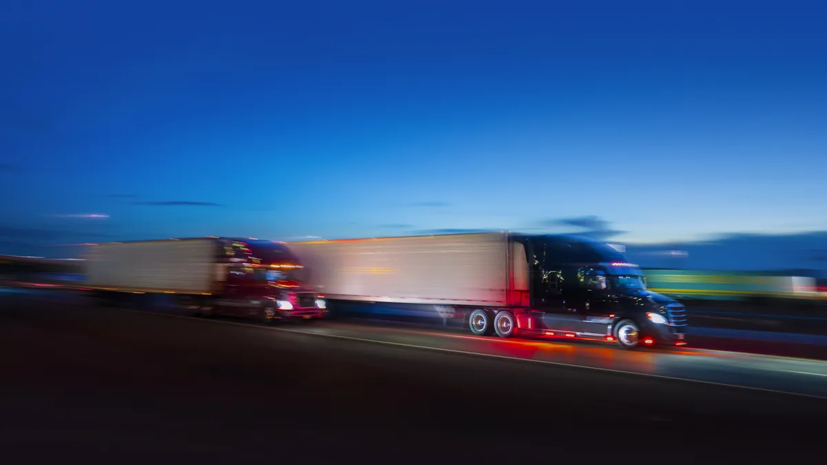 Trucks drive along a highway at twilight in a motion blur photograph.