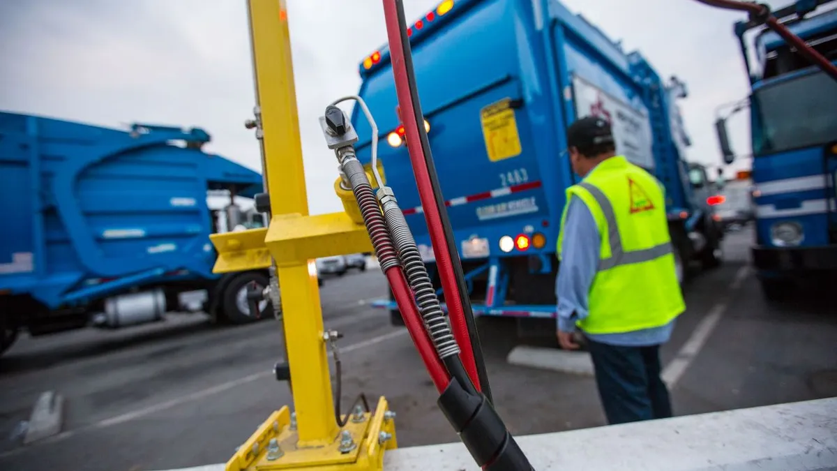 A fuel pump in focus in front of a line of waste trucks.