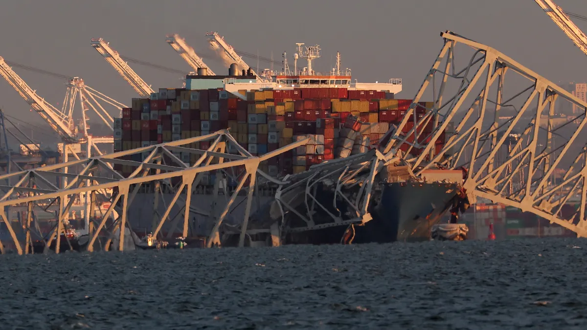 A ship floats with the cracked debris of a bridge hanging over it.