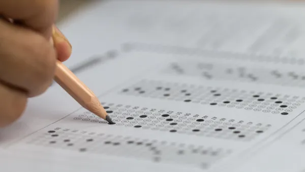 A close-up of a hand with a pencil filling in test answer sheet bubbles.