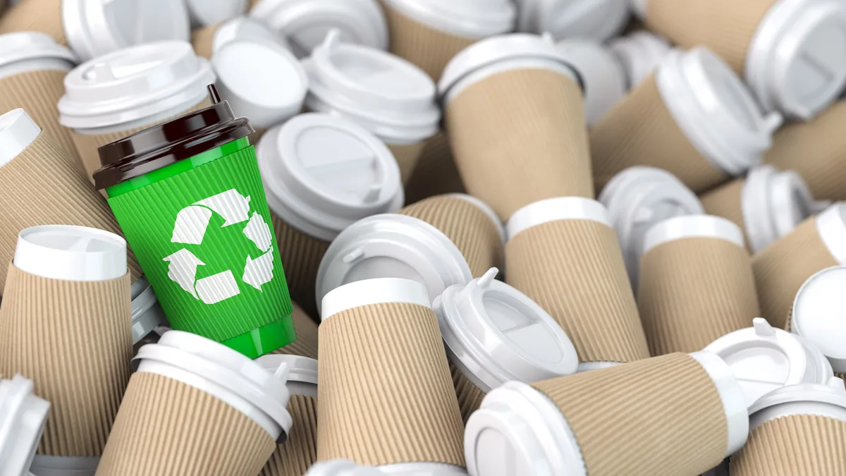 Dozens of paper beverage cups with natural-colored heat sleeves, and one cup with a green sleeve featuring a recycling symbol.