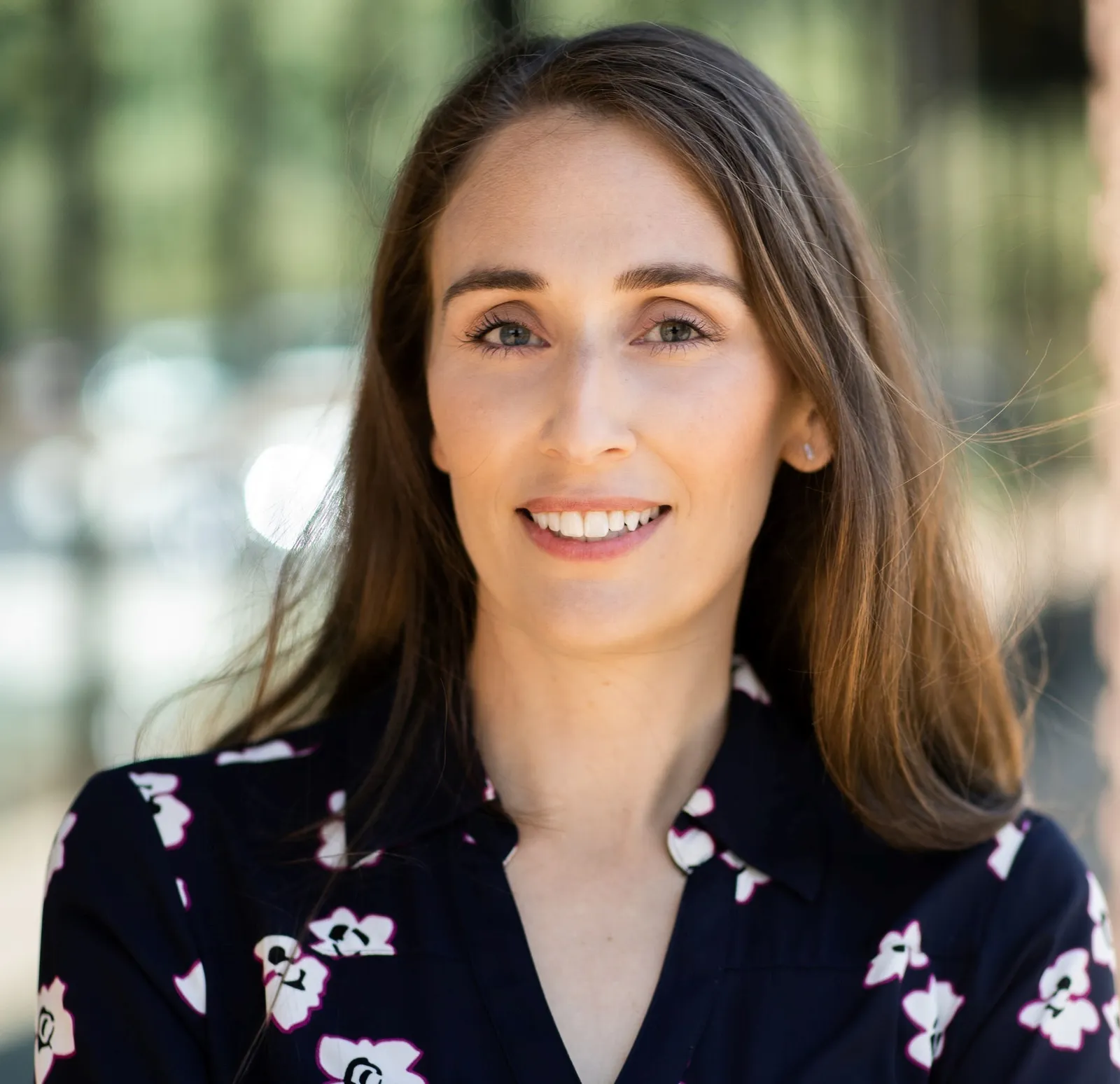 A headshot of someone wearing a floral dress with a blurred background.