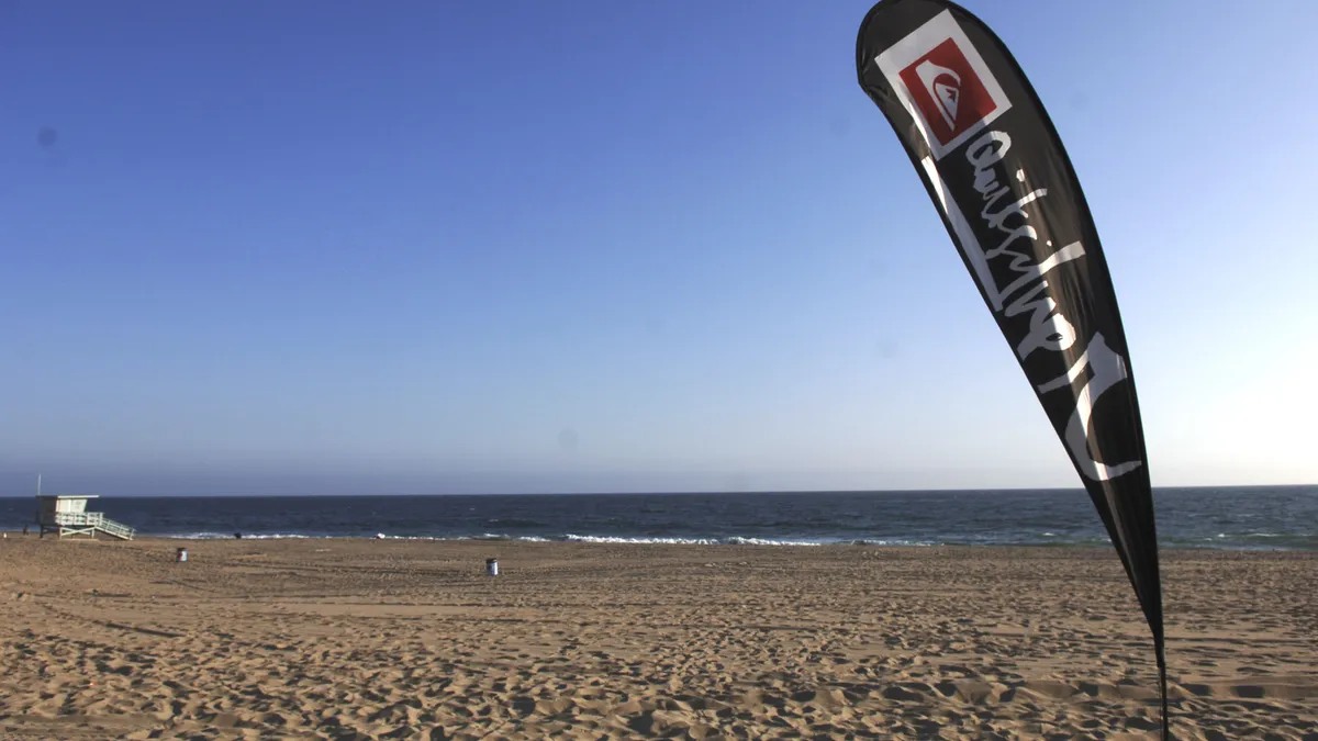 A Quiksilver flag is stuck in the sand on a beach.