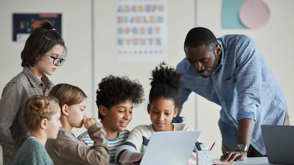 Diverse group of children with teacher using laptop together in modern school classroom