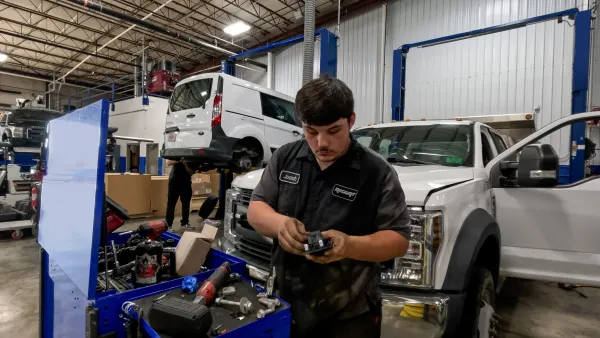 A technician inspects a part in the service department of Ricart Ford dealership in Columbus, Ohio in front of a white Ford F Series Super Duty truck.