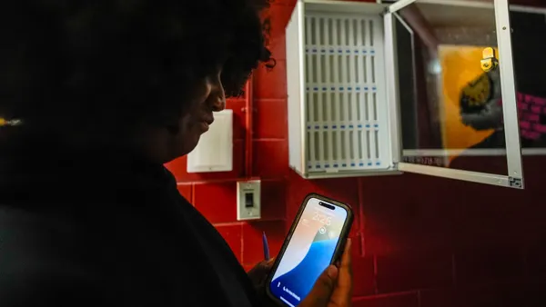 A person who is cast in a shadow holds a cellphone near a cellphone locker.