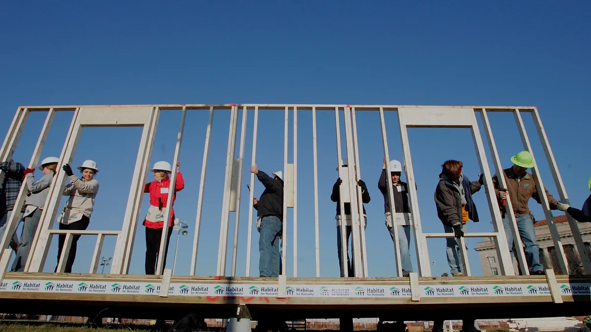 Volunteer workers raise a wooden framing wall on a Habitat for Humanity home under construction in Washington, DC.