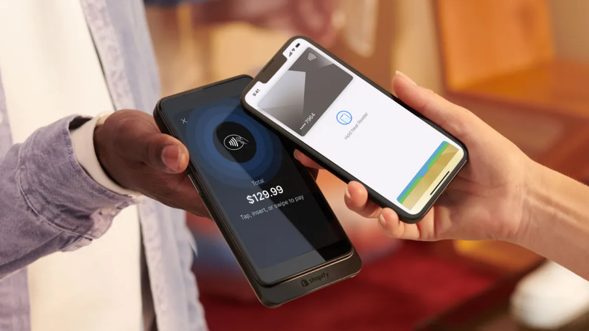 A shopper taps to pay with a smartphone as the store employee handles the transaction on a Shopify device.