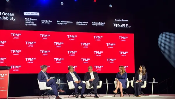 Four panelists sit in chairs next to each other on a stage with a red banner that says "TPM26" in the background.
