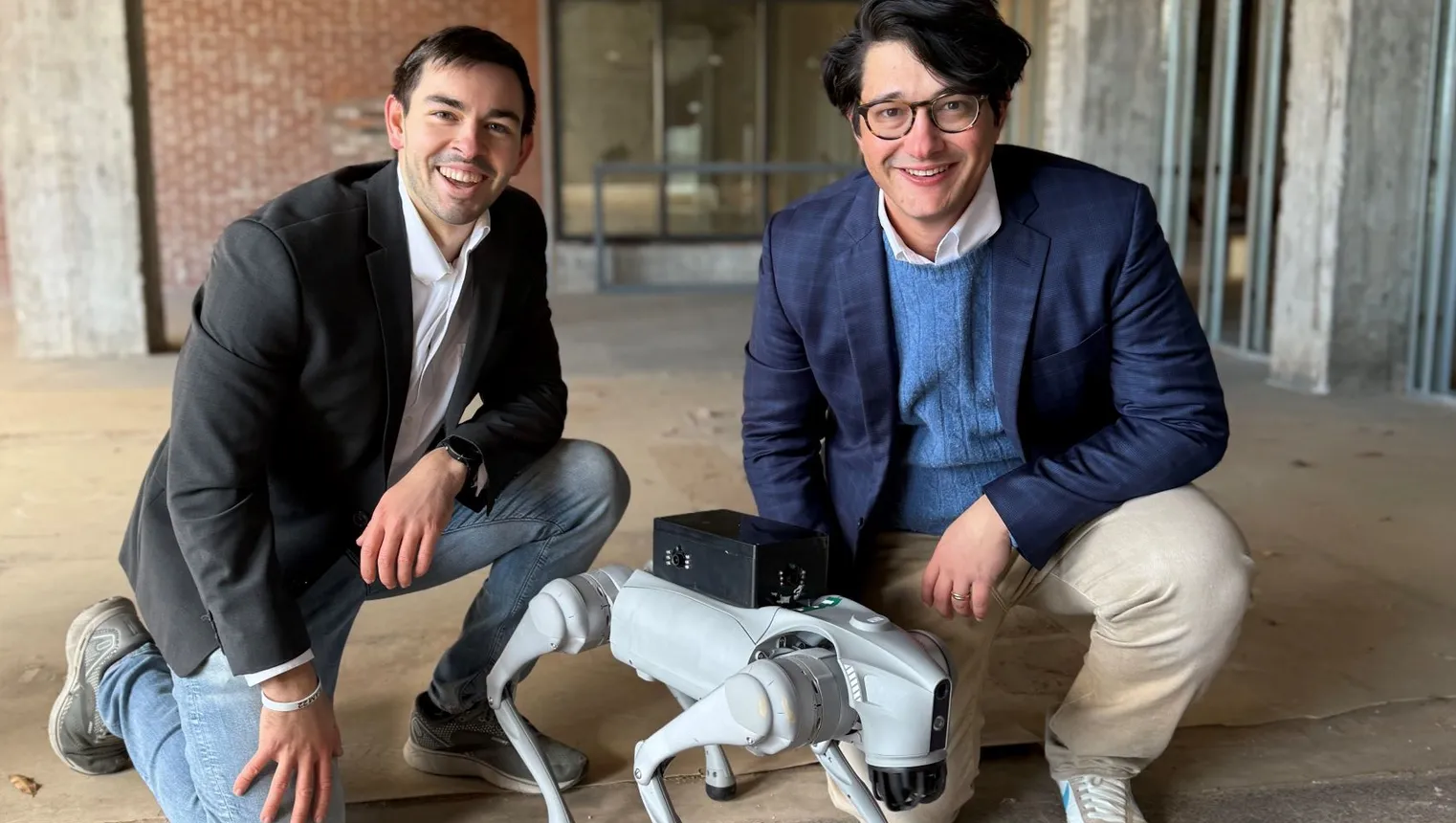 Two people are crouching next to a quadrupedal robot.