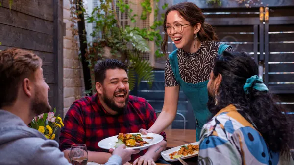 An image of three people sitting at a table as another person serves them food on white plates.