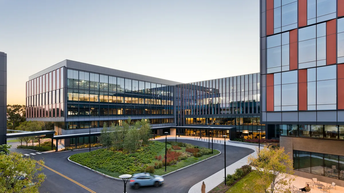 A glass building with a square roundabout with trees in the center.