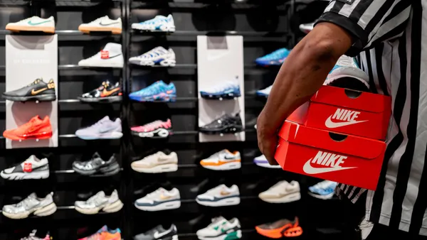 A Foot Locker employee carries a box in front of a wall display of sneakers.