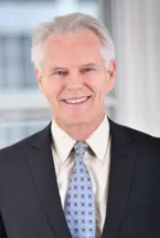 Man with white hair wearing a dark suit and light blue tie.