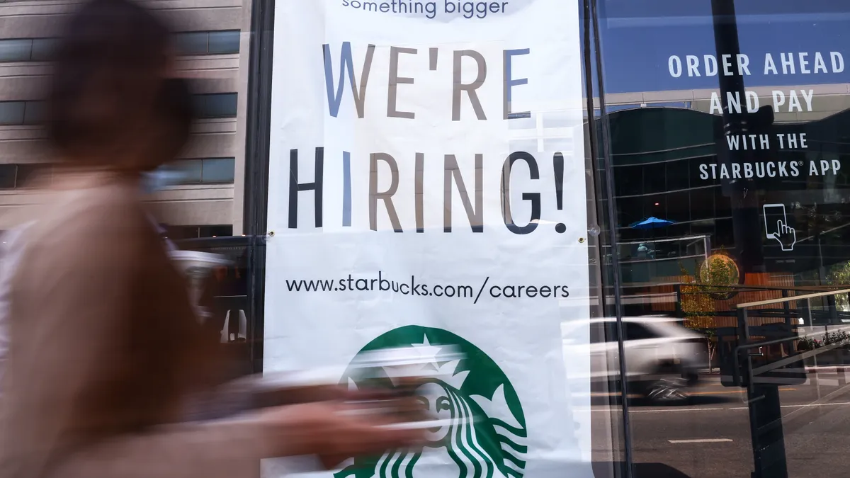 A sign saying "we're hiring!" hangs in a Starbucks window.