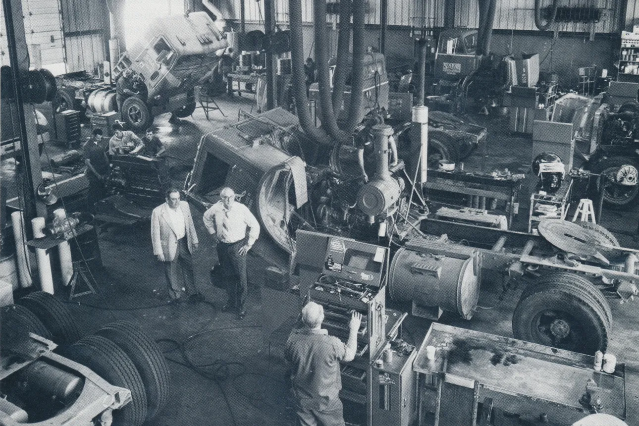 Six workers stand in a Saia truck maintenance facility in a black-and-white, aerial photo.