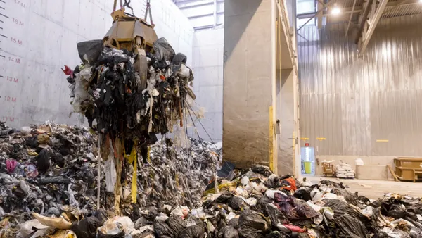 Mechanical claw hovering over pile of trash in industrial facility